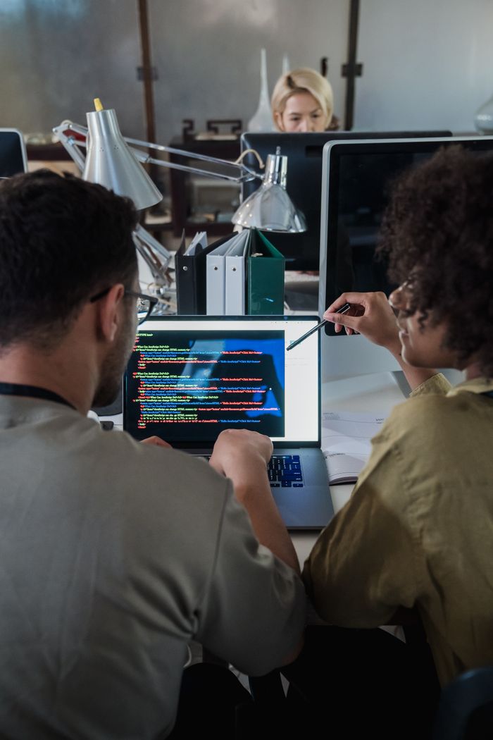 about-02 Two developers engage in software programming on a laptop in a modern office setting.